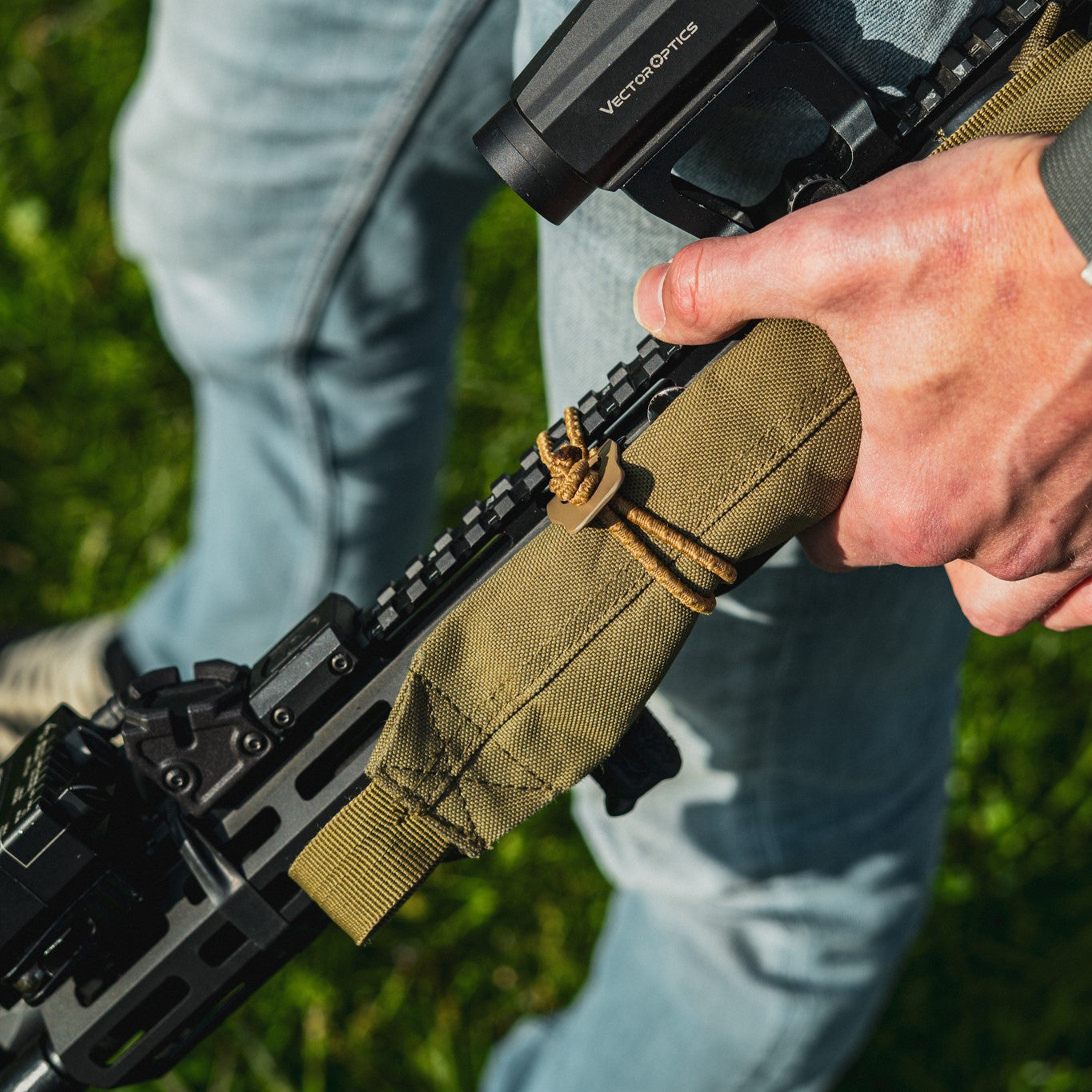 Person holding AR‑15 with BUSS 2.0 with a green sling against a grassy background